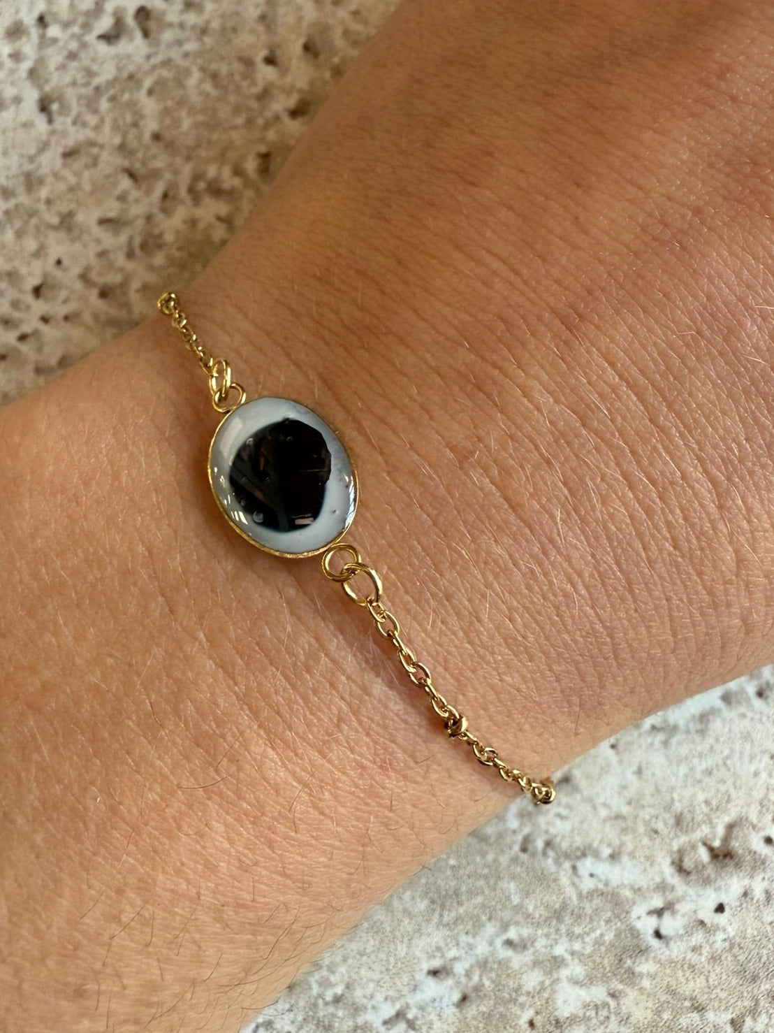 Bracelet doré avec médaillon en résine blanche et pétale noir porté au poignet.