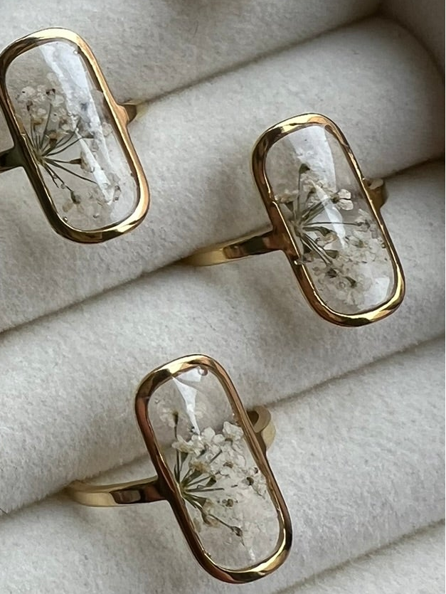 Bagues dorées avec fleurs séchées blanches incrustées dans de la résine transparente.